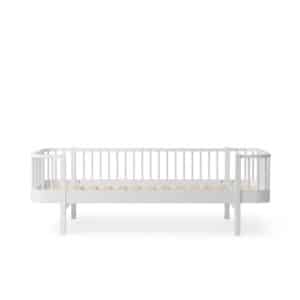 White wooden baby crib with vertical slats on all sides and a thin mattress base, empty of bedding.