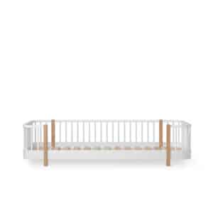 White baby crib with vertical slats and natural wood corner posts against a plain background.